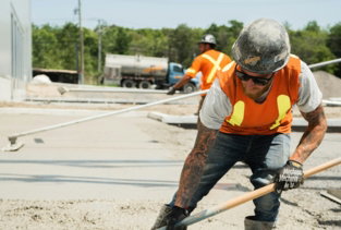 a man in an orange vest is shoveling concrete
